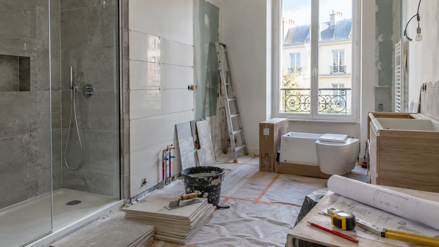 Salle de bain en rénovation avec carrelage, sanitaires, plans et matériaux de chantier.
